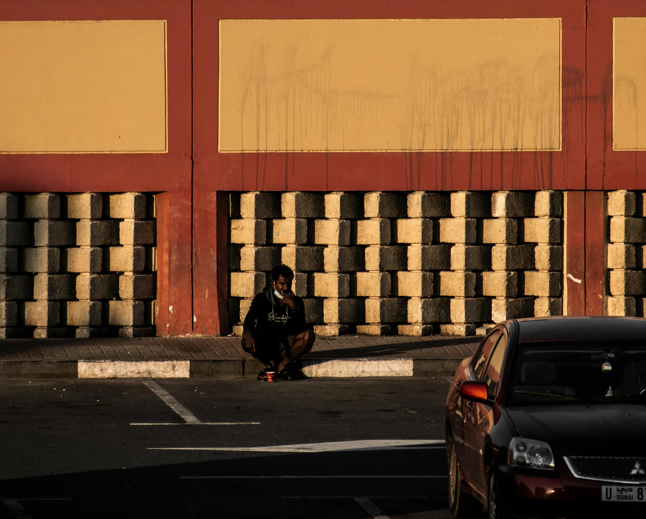 a man sits on the sidewalk next to a building with a red gate