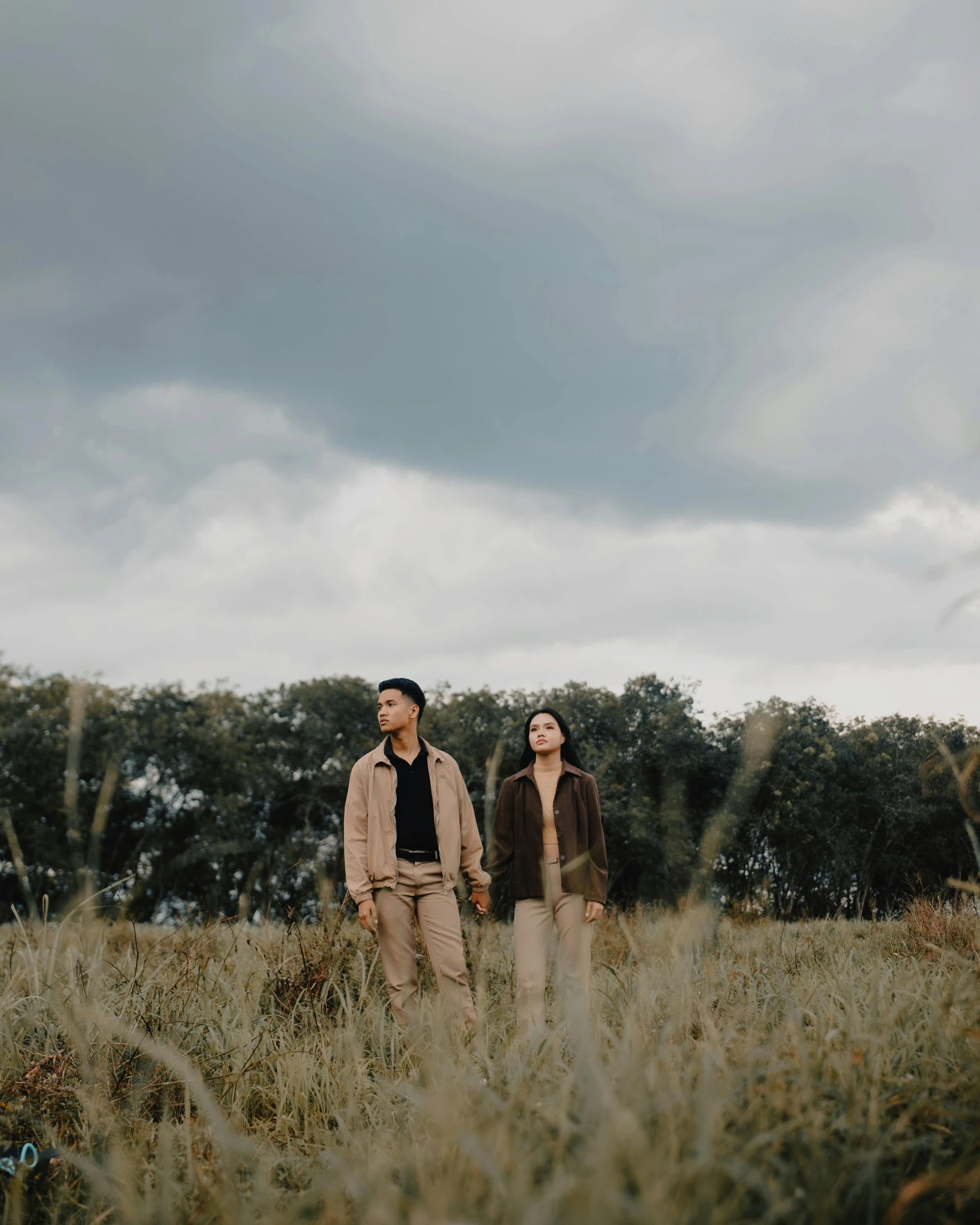 a man and woman walking through a field holding hands