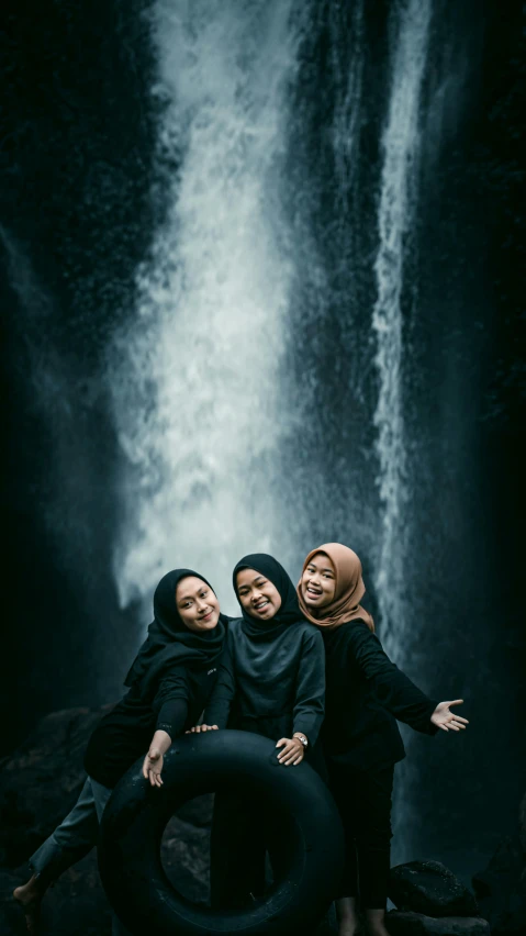 three girls in headscarves pose in front of a waterfall