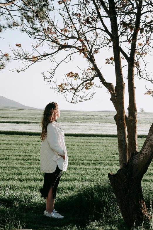 a woman standing by a tree in a large field