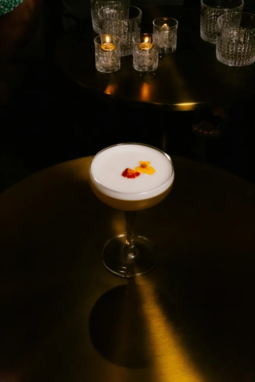 a white cocktail with a orange piece on the rim sitting in a black table next to lit candles