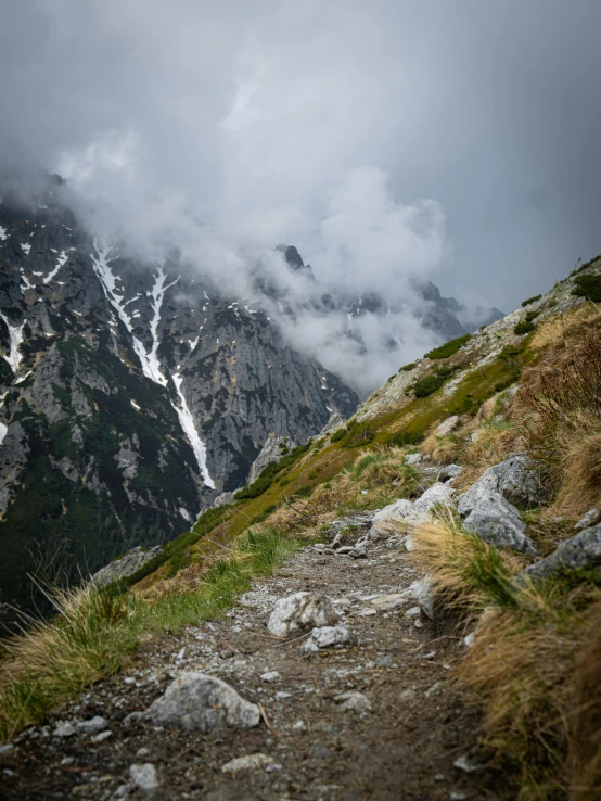 a path near the top of a mountain, leading up to a cloudy mountain