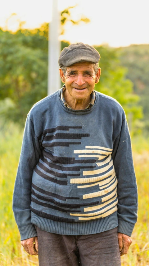 an older man wearing a grey and blue sweater and hat