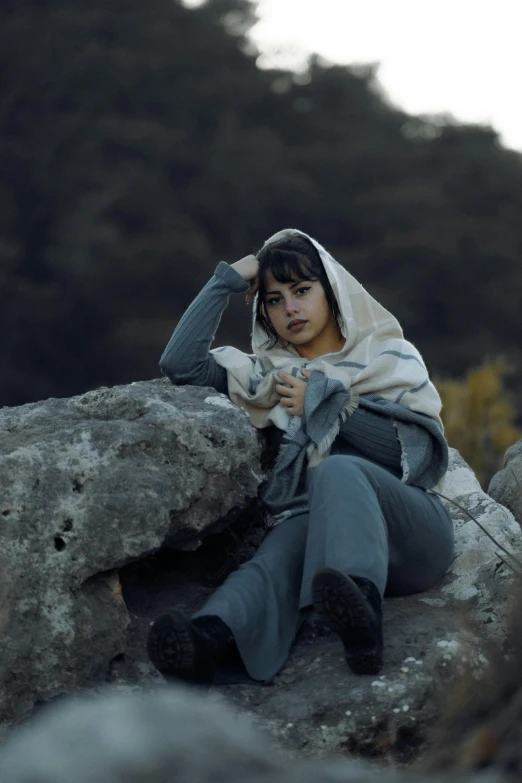 a boy is sitting on a rock with a hood over his head