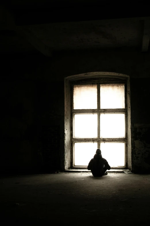 man sitting in the dark behind a window with bright light