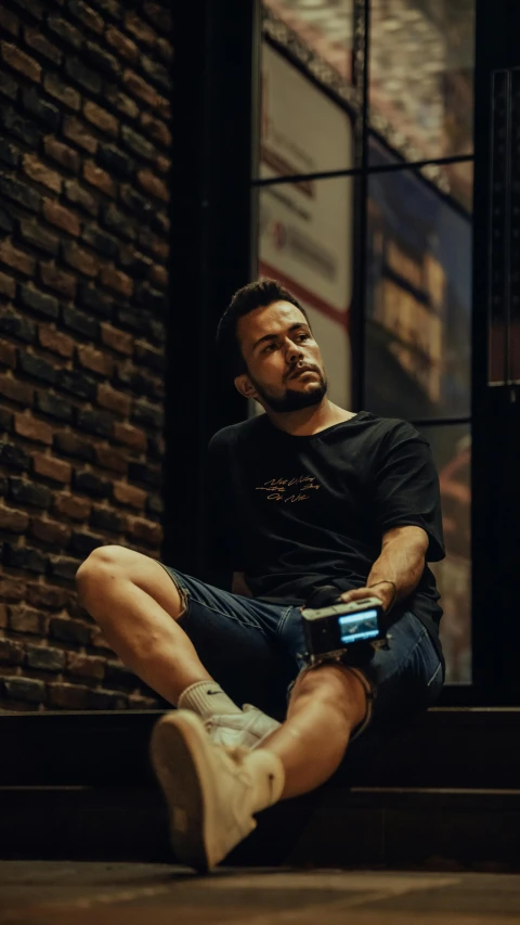 a man is sitting in front of a brick wall