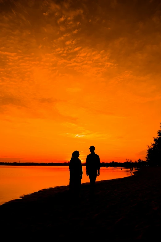 a couple stand on the edge of a lake as the sun sets