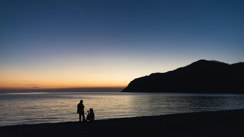 two people are standing on the edge of the ocean at sunset