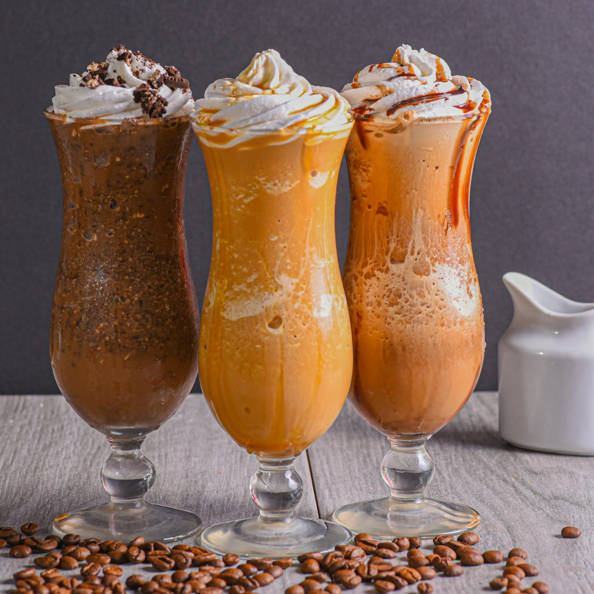 three glasses filled with dessert type drinks next to a pitcher and peanuts