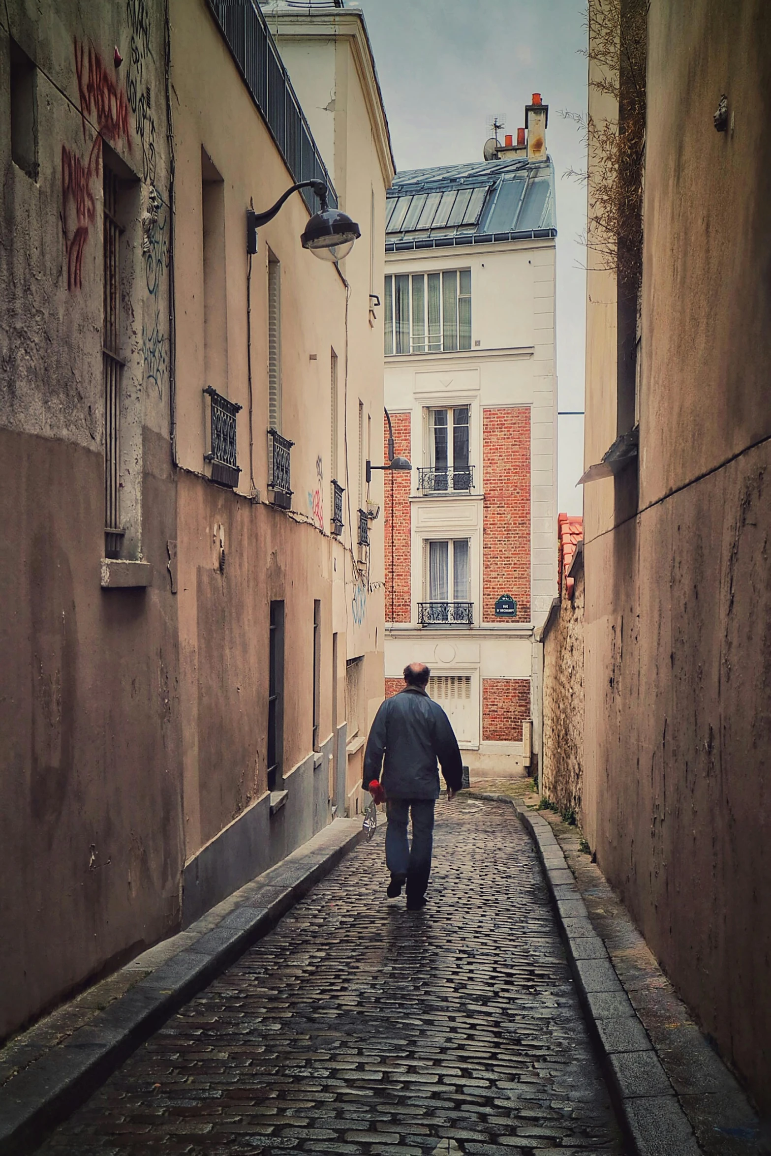 two people are walking down the narrow cobblestone street