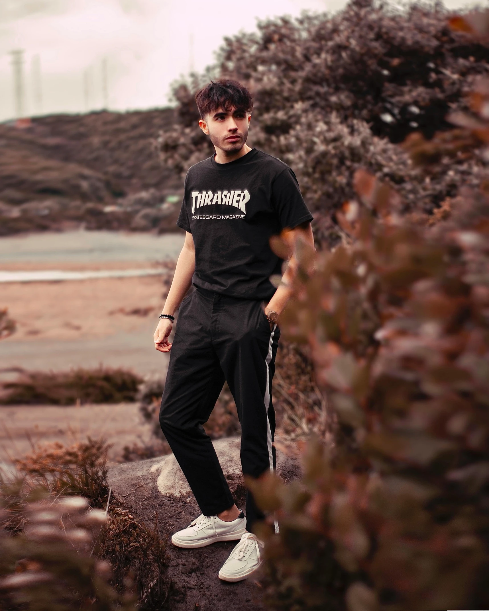 a man in black and white pants stands by a bush