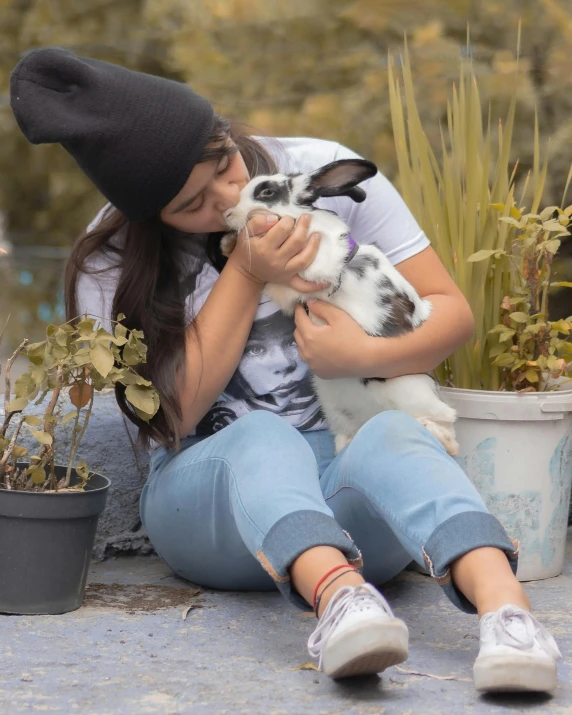 the girl is sitting on the curb hugging the small rabbit