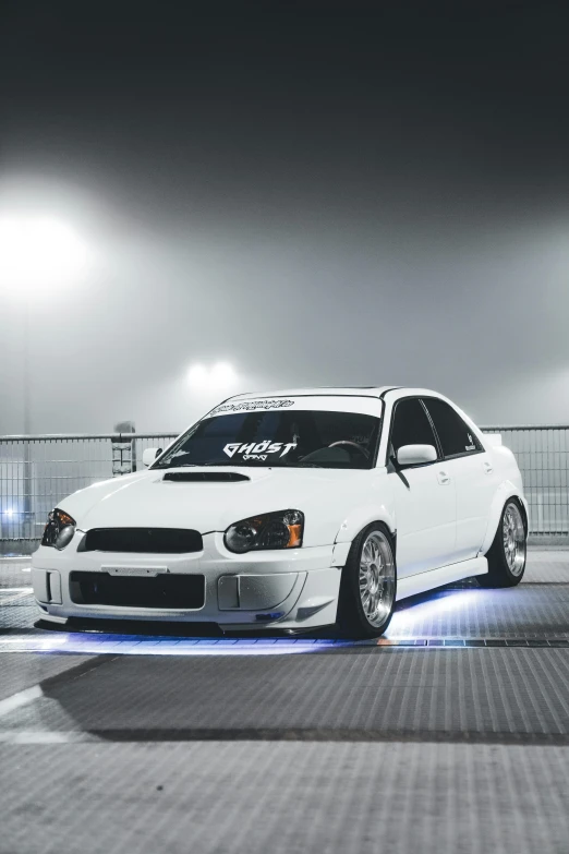 a white car with a black license plate on a parking lot at night