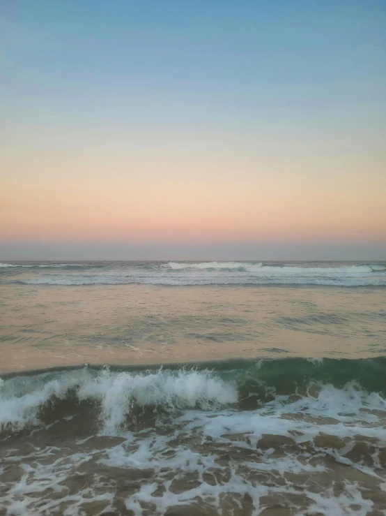 sunset, ocean waves and a white surfboard on the shore