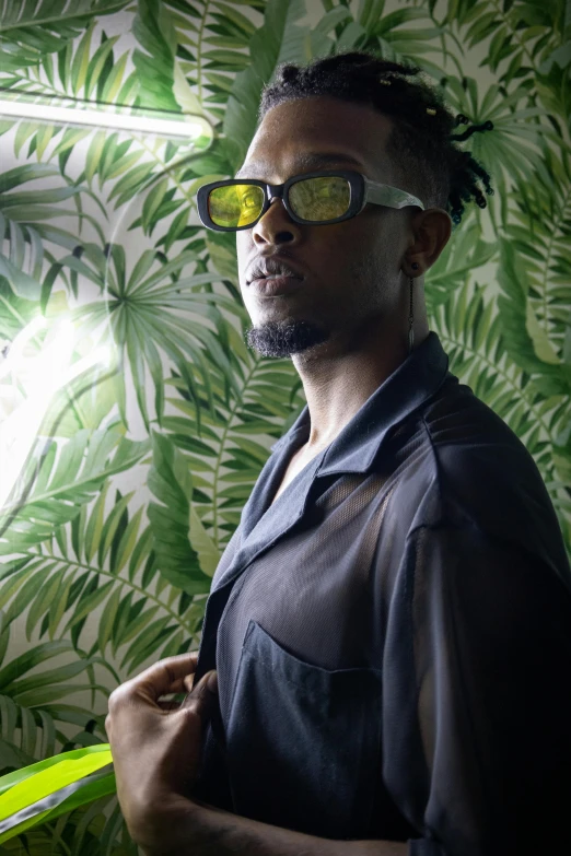 a man wearing large glasses in front of a jungle - themed wall