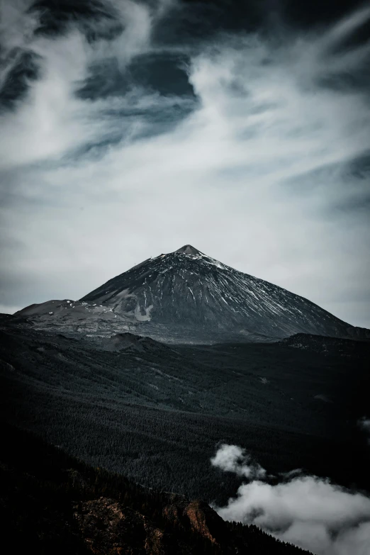 the top of a mountain in the dark with clouds around it