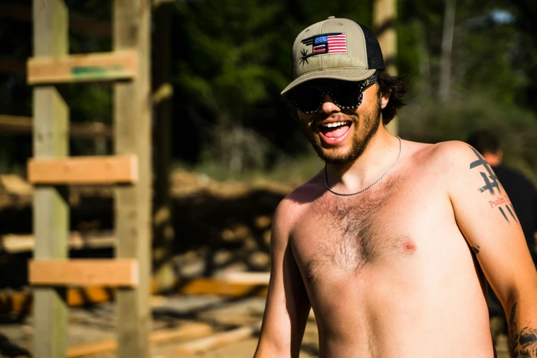 a shirtless man with an american flag hat, sunglasses and a cross on his chest
