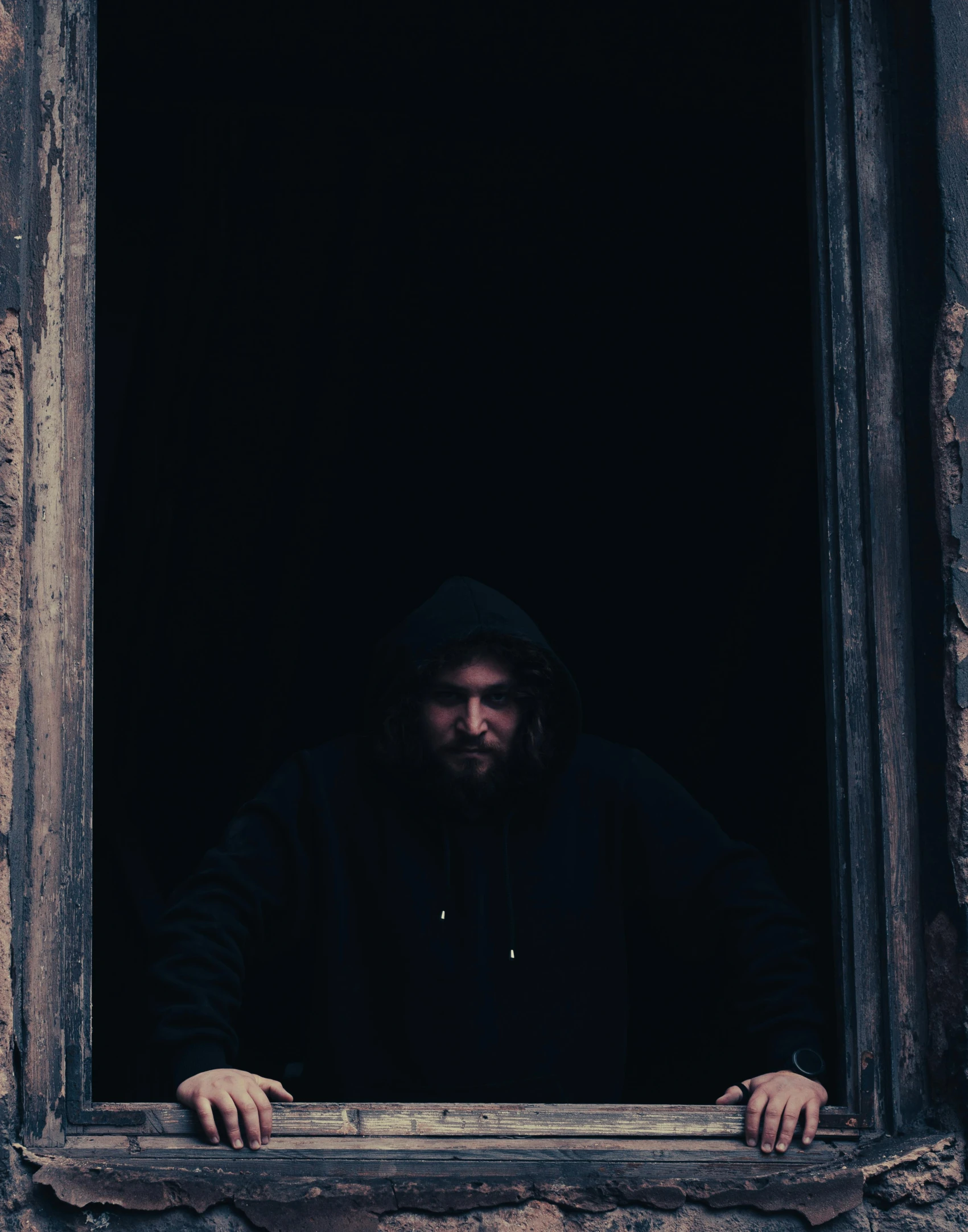 a bearded man in a black hoodie, standing in an open window