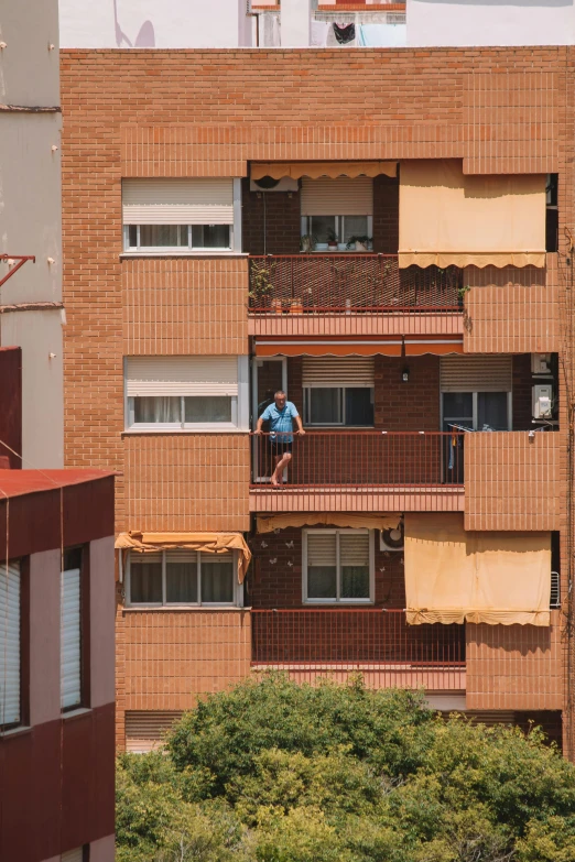 a man standing on the balcony of an apartment building in front of trees