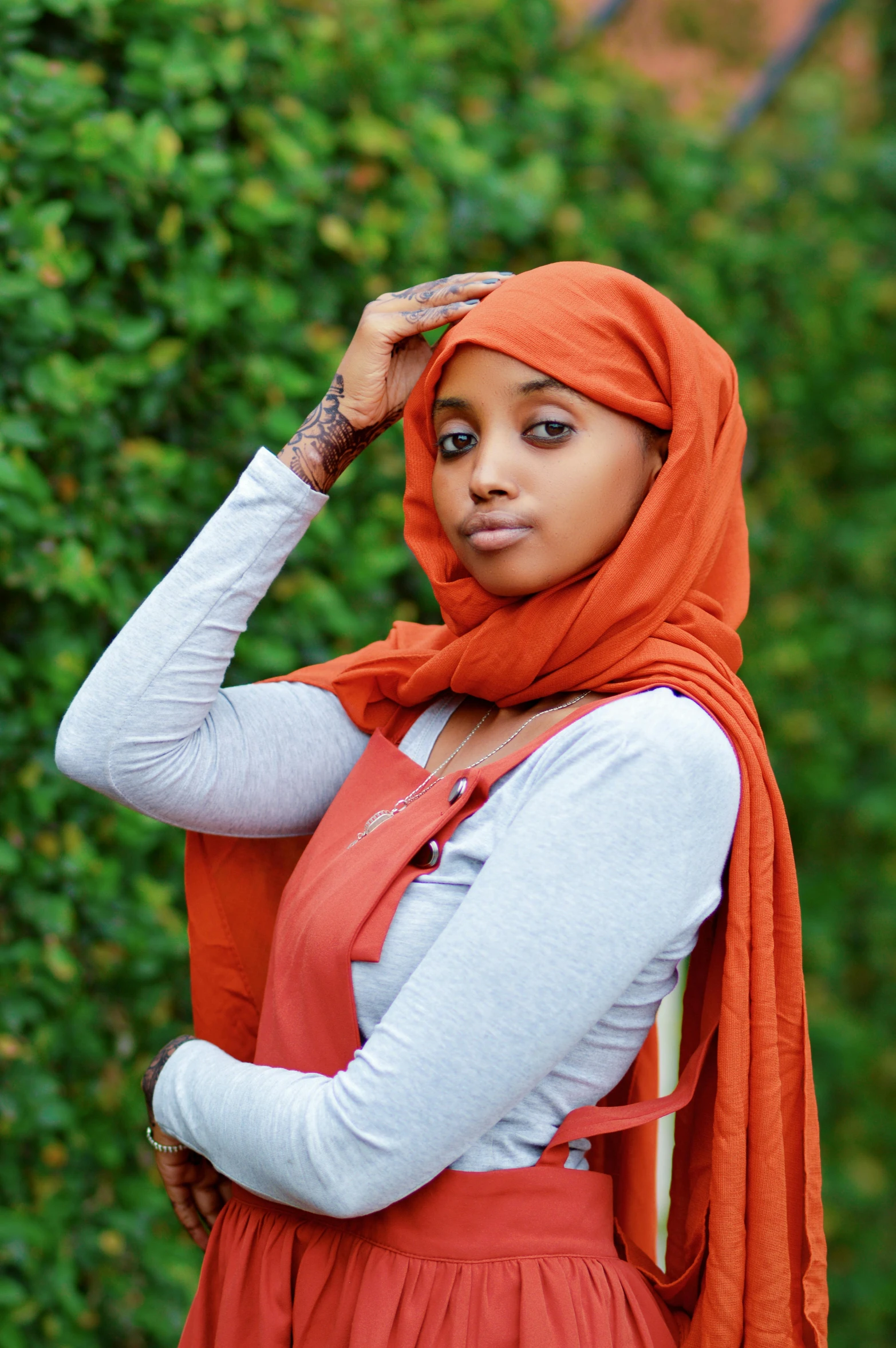 a woman with an orange scarf standing in front of some bushes