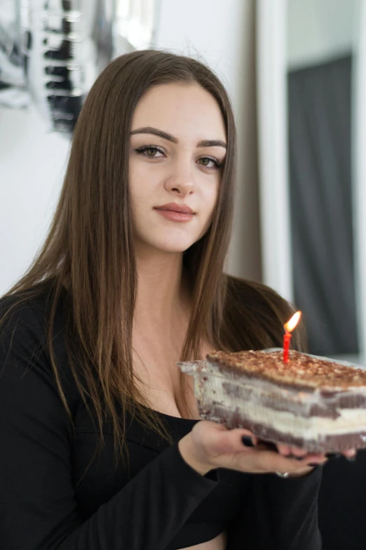 a young lady is holding up a cake with a candle