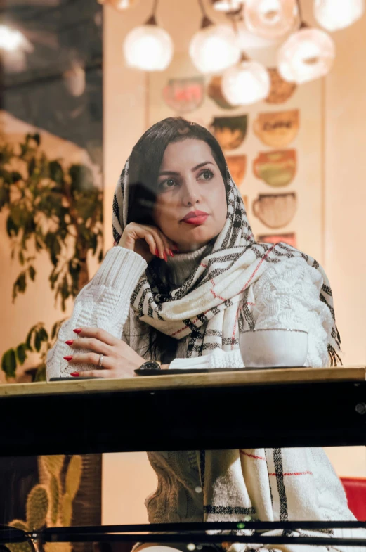 a woman sits with her hand on her head and looks out a window at a plant