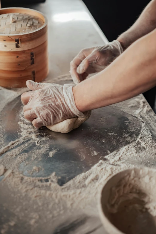 a man in a black shirt and gloves kneading dough