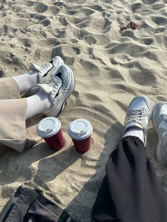 the legs of a person on sand with two cups