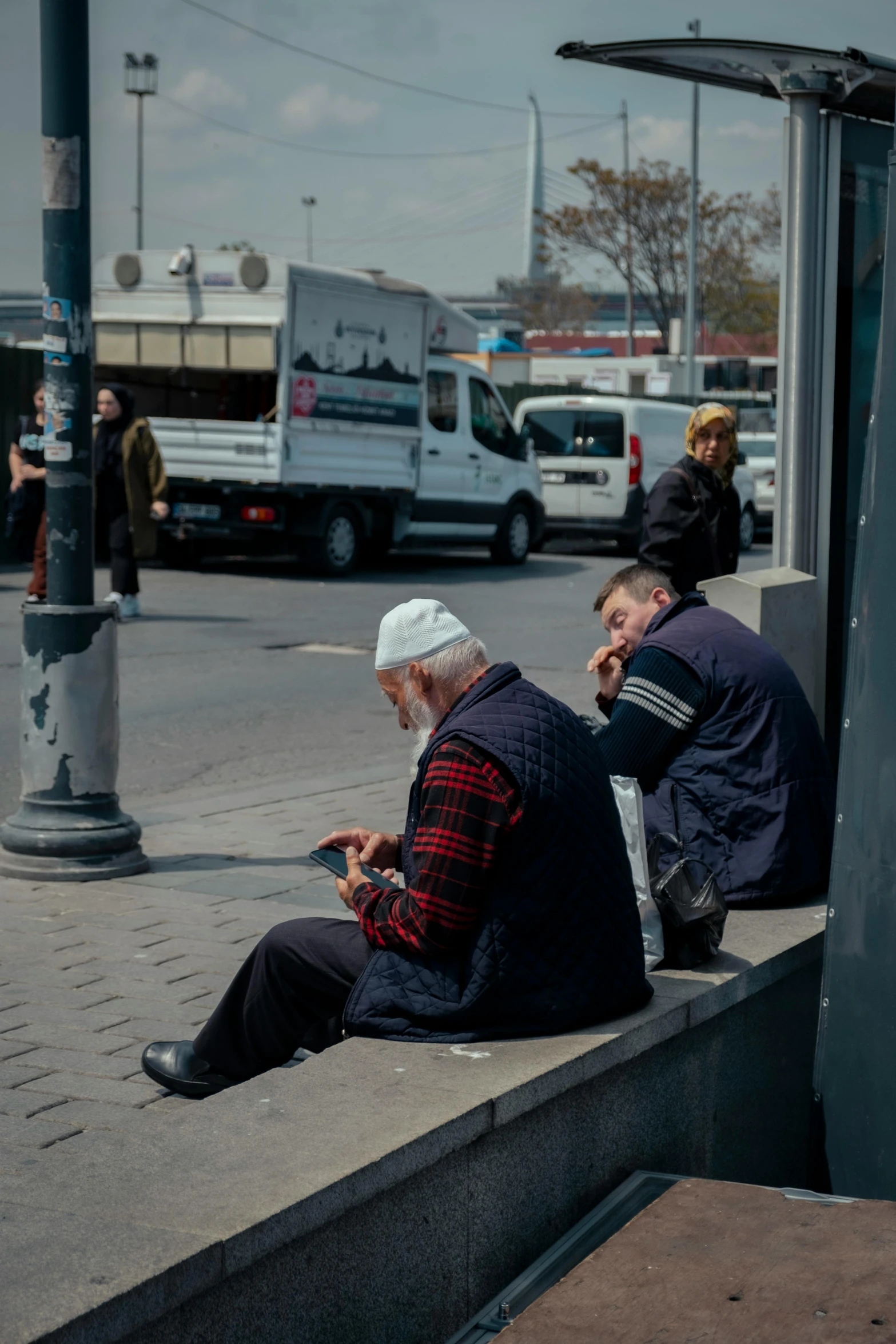 two men sit on the curb while looking at their phones