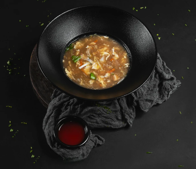 a black bowl full of soup next to a little cup of soup