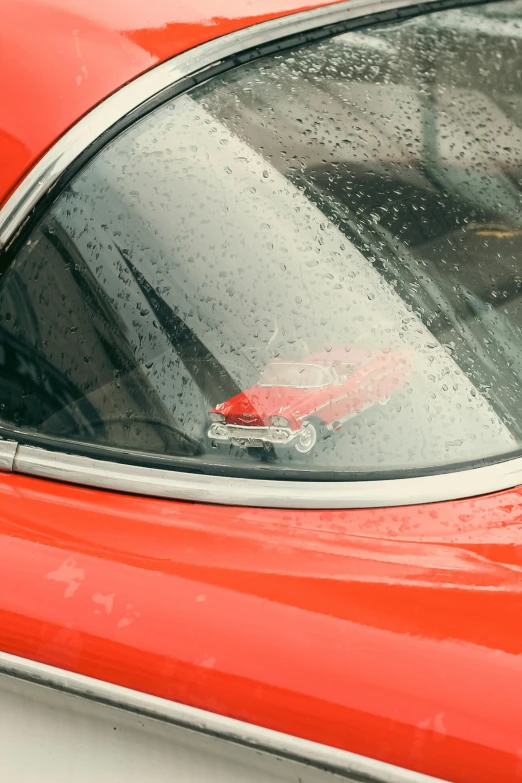 a red car with raindrops on it's window and rear view mirror