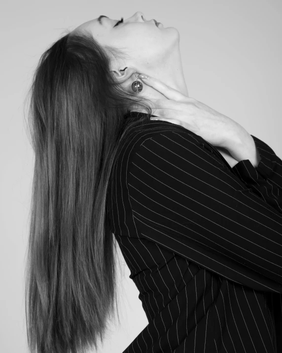 a woman with long hair is bending her head while she holds her hands up to her chest