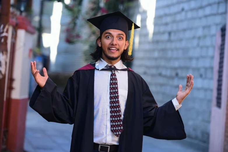 a man dressed in a graduation gown and cap, holding his hands out