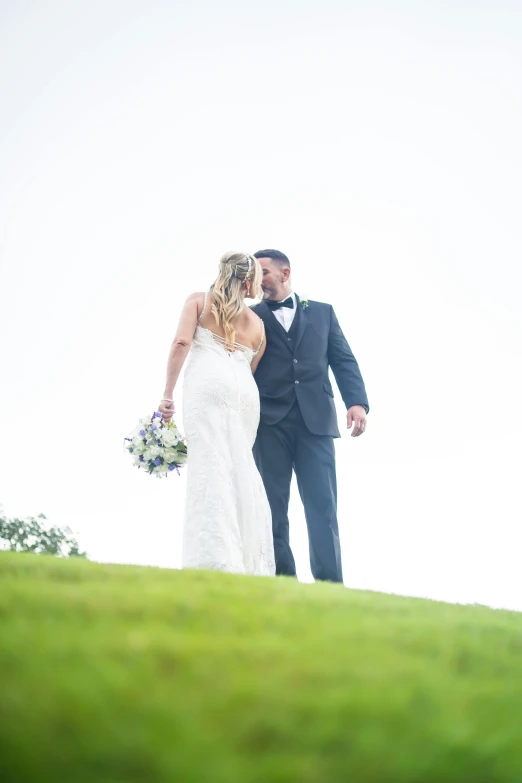 a bride and groom on a hill top with the sky behind them