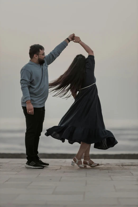 a man and woman dance on a stone sidewalk near the ocean