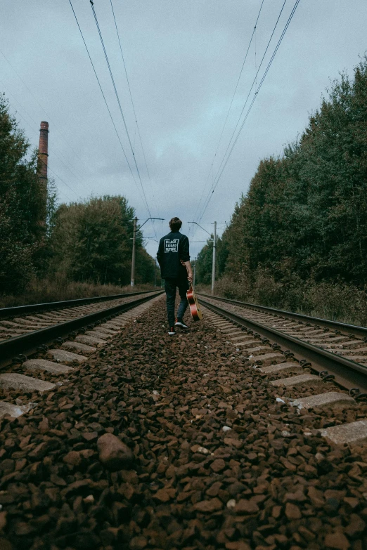 a man with a backpack and a toy walk down a railroad track
