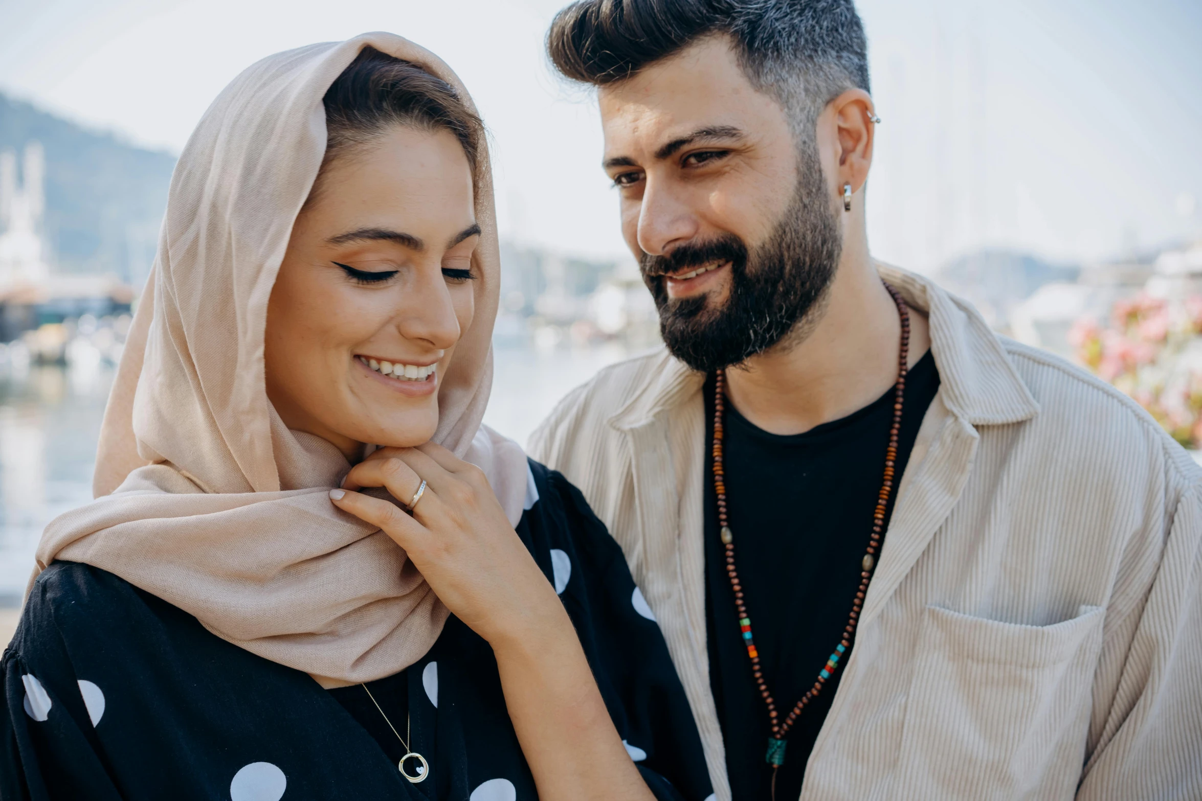 a man and woman wearing scarves pose together in front of the water