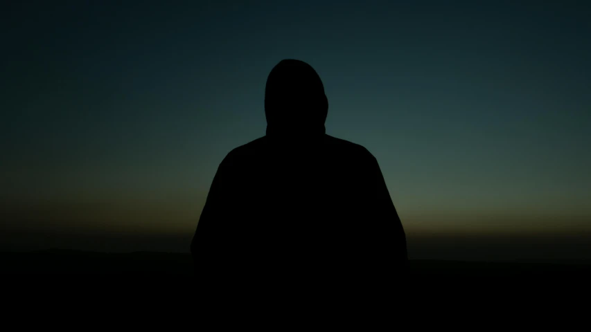 a person standing in the dark, wearing a hood