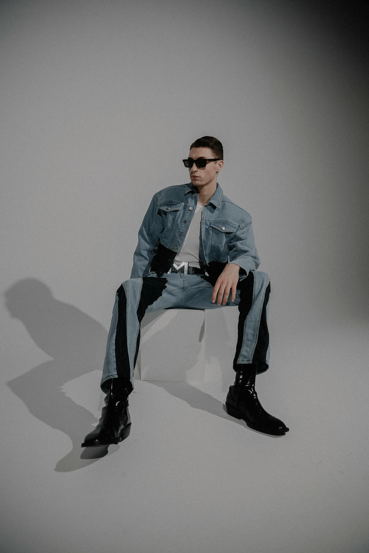 a man wearing a jean jacket and sunglasses sitting on a chair