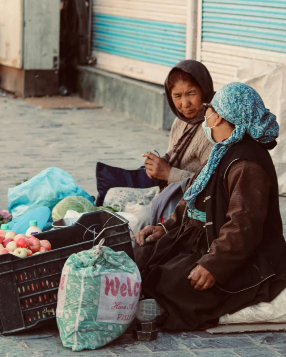 two women are sitting on a street with produce