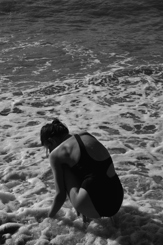 a woman kneeling in the sand near a body of water