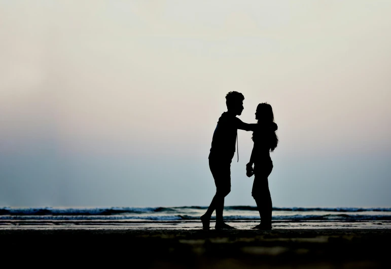 a silhouette of two people on the beach facing each other