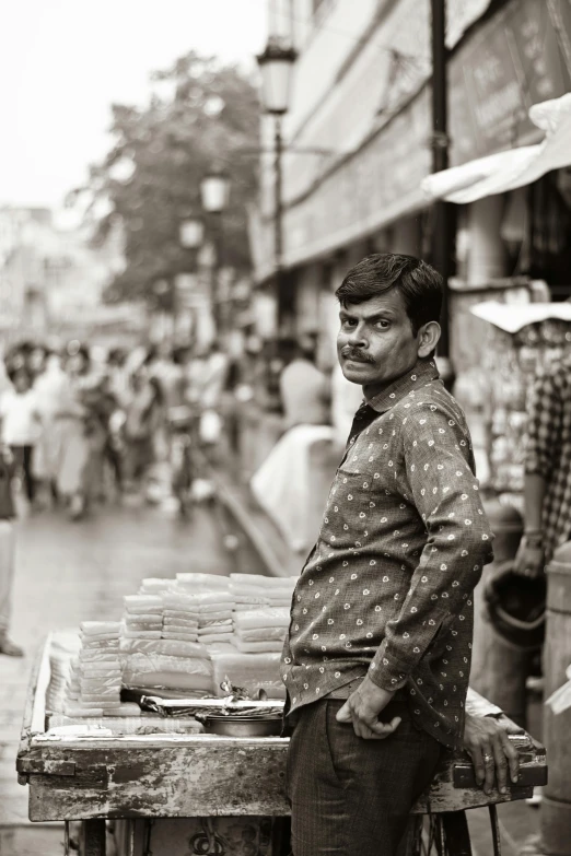 a man is standing near a wooden table that contains paper in front of him