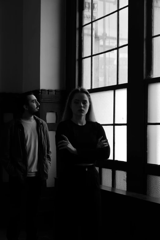 two people stand in a dark room with tall windows