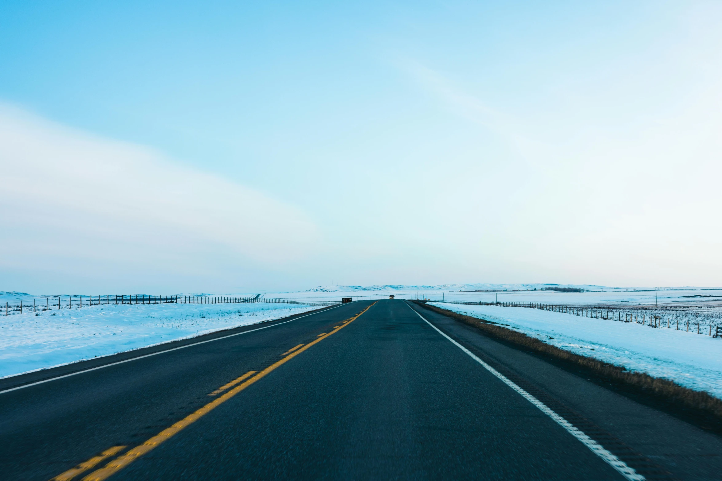 a long road in a snowy field next to a blue sky