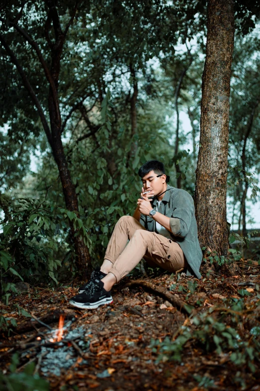 a man sitting on the ground next to a fire in the woods