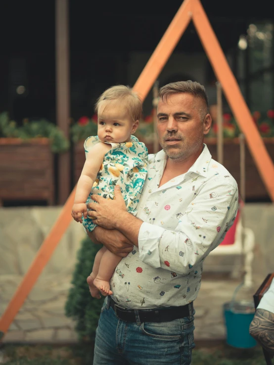 a man holding a toddler outside with flowered pots behind him