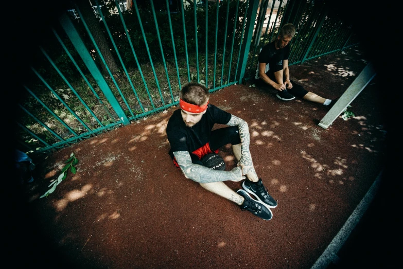 two boys sitting on the ground next to a fence