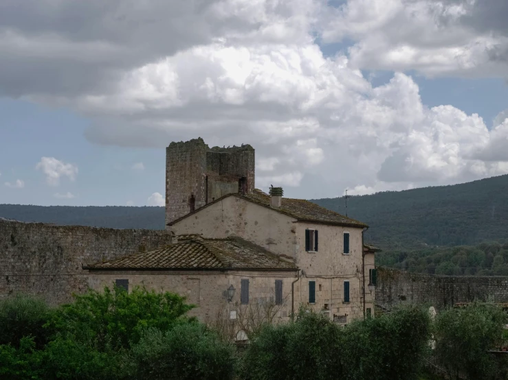 an old building with blue shutters and green bushes near a mountain range