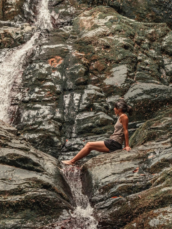 a man sitting on top of a rock next to a waterfall